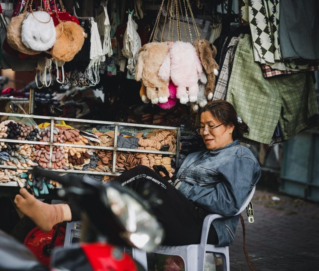 Woman vendor relaxing amidst a variety of garments and plush toys in Kon Tum, Vietnam.